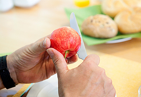 Hände, die einen Apfel mit einem Messer auseinander schneiden.